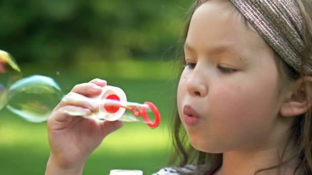 Närbild. Söt förskola flicka entusiastiskt blåser såpbubblor. Mot bakgrund av färsk sommar grönska. — Stockvideo