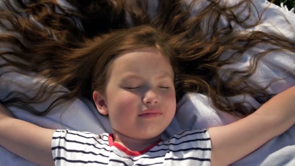 Close-up. Criança deitada em cobertor fazendo piquenique no parque de verão. Menina abriu os braços para os lados. — Vídeo de Stock
