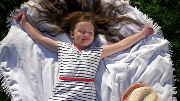 夏の公園でピクニックをする毛布の上に寝そべっている子供。女の子は腕を横に広げ. — ストック動画