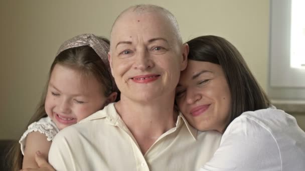 An adult daughter and little granddaughter hug a sad elderly woman who has gone bald after chemotherapy. Love, care and support in the family of a cancer patient. — Stock Video