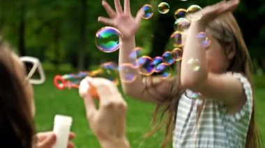 Genç bir kadın sabun köpüğü üflüyor. 6 yaşındaki kızı mutlu bir şekilde gökkuşağı kabarcıkları yakalıyor. Aile tatili.