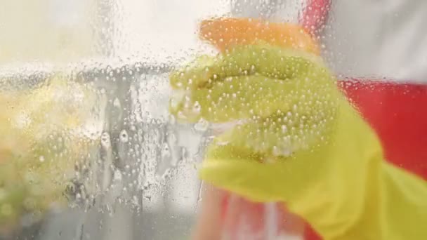 Manos femeninas en guantes amarillos limpiando el cristal de la ventana con trapo y detergente en aerosol. Lavado de ventanas con spray. — Vídeo de stock