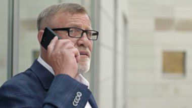 Modern ofis binasının dışında akıllı bir telefonla konuşan kıdemli bir işadamının portresi. Başarılı bir iş adamı..