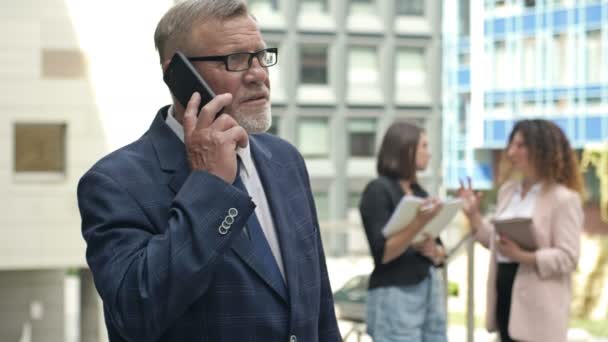Portrait d'un homme d'affaires âgé parlant sur un téléphone portable dans la cour d'un grand centre d'affaires. — Video