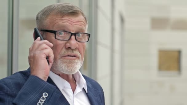 Portret van een senior zakenman die praat met een smartphone buiten het moderne kantoorgebouw. Succesvolle zakenman. — Stockvideo