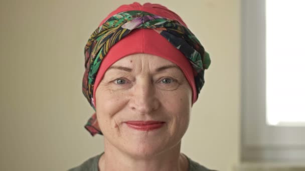 Portret van een oudere vrouw met kanker. Doet een sjaal af van een kale kop. Alopecia als gevolg van chemotherapie. De vrouw glimlacht ondanks de pijn, angst en wanhoop. — Stockvideo