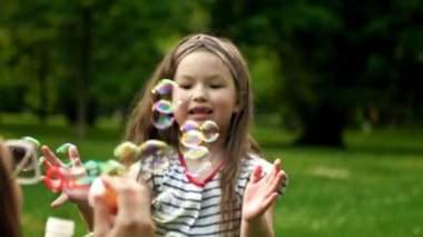 6 yaşındaki bir kız, annesinin üflediği gökkuşağı baloncuklarını mutlulukla yakalar. Aile tatili.