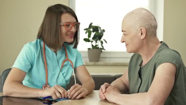 Starsza kobieta u onkologa, konsultacja w sprawie wyników chemioterapii, dobre wieści. Młoda lekarka z uśmiechem łagodzi i wspiera pacjenta. — Wideo stockowe