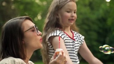 Genç bir kadın sabun köpüğü üflüyor. 6 yaşındaki kızı mutlu bir şekilde gökkuşağı kabarcıkları yakalıyor. Aile tatili.