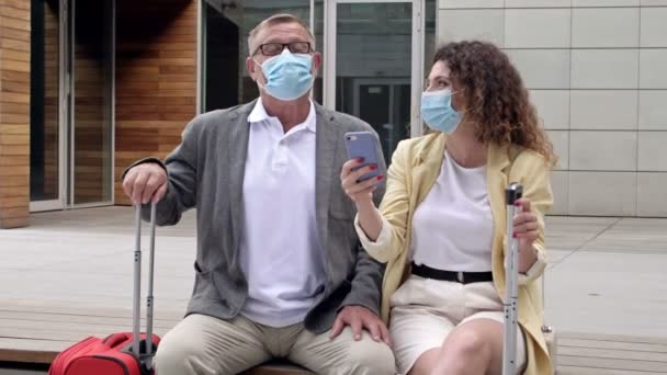 Beau couple d'âge mûr attend leur vol dans la salle d'attente. Masques médicaux. Voyages, tourisme pendant l'épidémie de coronavirus. — Video