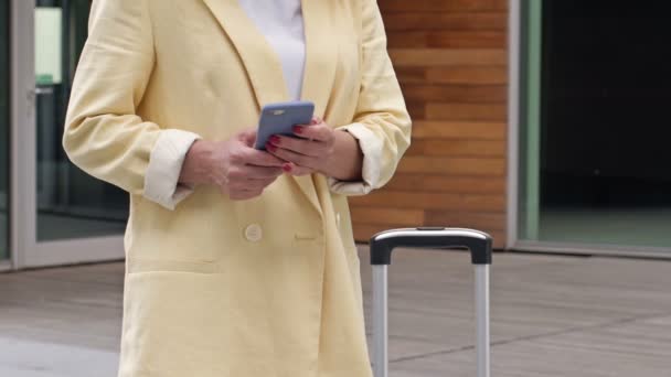 Geschäftsfrau mit Koffer benutzt Handy und wartet auf jemanden. — Stockvideo
