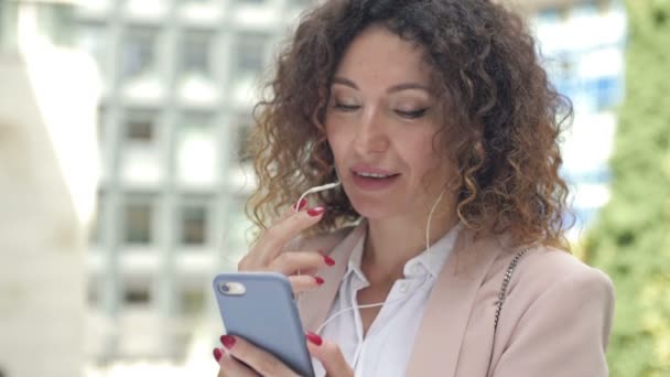 한 사업가 가 거리에서 전화와 헤드폰을 사용하여 일할 수있는 모습. 밖으로 나가서 밖에서 일하 십시오. 새로운 정상적 인 생활. — 비디오