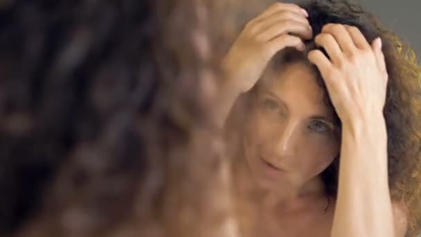美しい中年女性は鏡の中で彼女の豪華な髪を調べます.彼女は白髪が気になる. — ストック動画