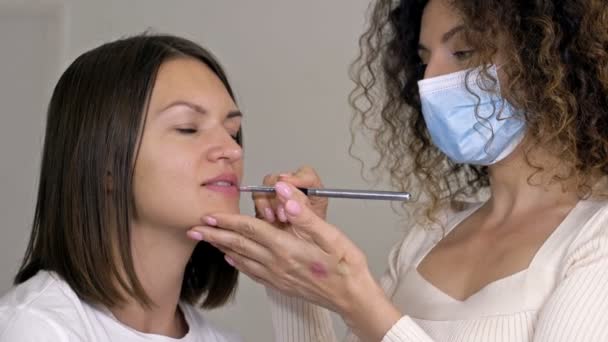 Ein Visagist trägt mit einem speziellen Pinsel Lippenstift auf die Lippen einer jungen Frau auf. Professionelles Make-up. — Stockvideo