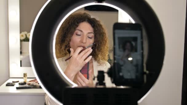 Välvårdad, medelålders skönhetsbloggare förklarar hur man applicerar ögonskugga. Kvinna filmar processen med en videokamera. — Stockvideo