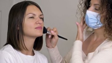 Makyaj sanatçısı güzellik salonundaki fırçayı kullanarak güzel kadınların yüzüne pudra sürüyor..