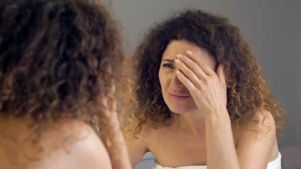 Mujer de mediana edad lamentablemente examina sus arrugas en el espejo. — Vídeos de Stock