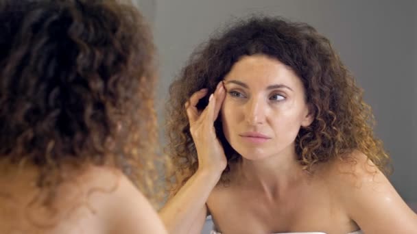 Mujer de mediana edad lamentablemente examina sus arrugas en el espejo. — Vídeos de Stock