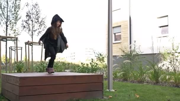 Uma menina de 6 anos joga no pátio de um prédio de apartamentos com um traje de morcego. As crianças adoram Halloween. — Vídeo de Stock