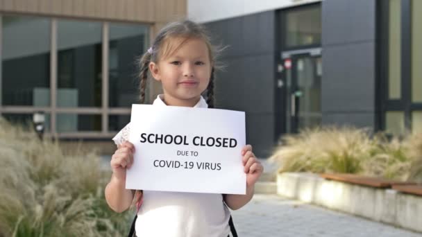 Söt liten skolflicka med flätor står med en affisch SKOLA ÄR CLOSED DUE att COVID-19 VIRUS. — Stockvideo