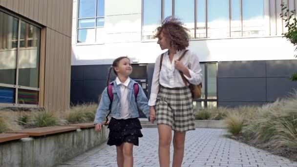 Sırt çantalı, farklı yaşlarda iki kız öğrenci el ele tutuşarak okula gidiyor. Büyük kız kardeş küçük olanı okula götürür. Okula geri dön.. — Stok video