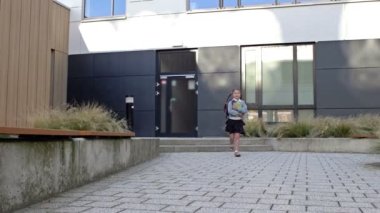 Bir ilkokul öğrencisi okuldan sonra eve koşar. Okul binasının arka planında at kuyruklu ve sırt çantalı küçük bir kız koşuyor..