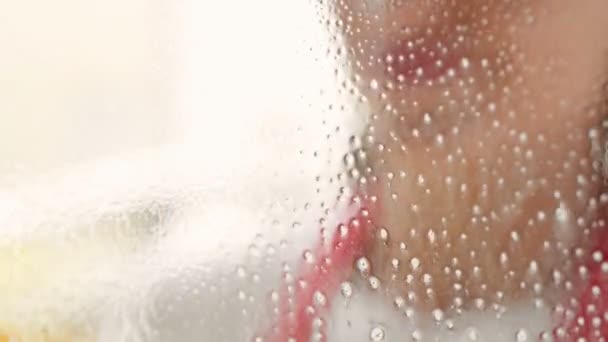 Manos femeninas en guantes amarillos limpiando el cristal de la ventana con trapo y detergente en aerosol. Concepto de limpieza. — Vídeo de stock