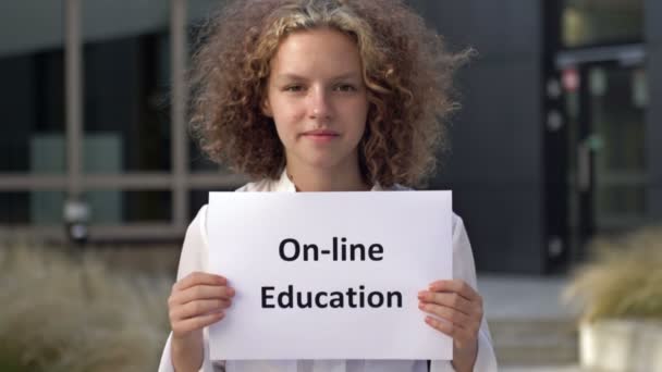 Carino ragazza adolescente si trova con un poster ISTRUZIONE ONLINE vicino all'edificio scolastico. — Video Stock