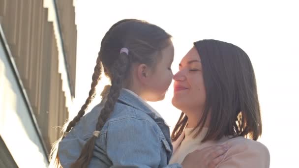 Young woman lovingly hugs a girl with pigtails 6-7 years old. Meeting or parting of mom and daughter. Mothers Day. — Stock Video