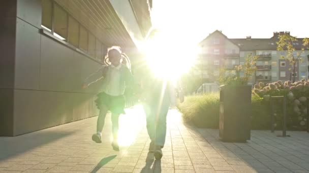 Eine junge Frau führt ihre sechs bis sieben Jahre alte Tochter an der Hand zur Schule. Das Mädchen mit den Zöpfen hüpft fröhlich los. Zurück zur Schule. — Stockvideo