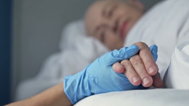 Pflegende Hand einer Krankenschwester in Schutzhandschuhen, die die Hand einer kranken Person hält. Liebe, Mitgefühl und Unterstützung. Nahaufnahme. — Stockvideo