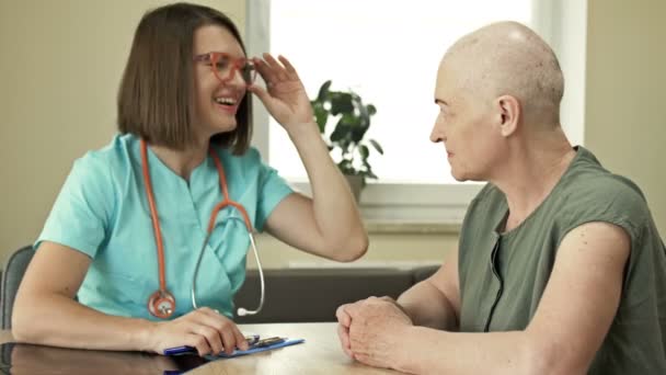 Een oudere vrouw bij de oncoloog, consultatie over de resultaten van chemotherapie, goed nieuws. Jonge vrouwelijke arts met een glimlach kalmeert en ondersteunt de patiënt. — Stockvideo