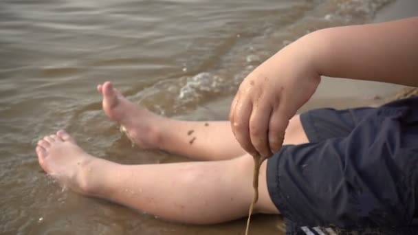 Gelukkige jongen spelen met zand aan de oever — Stockvideo