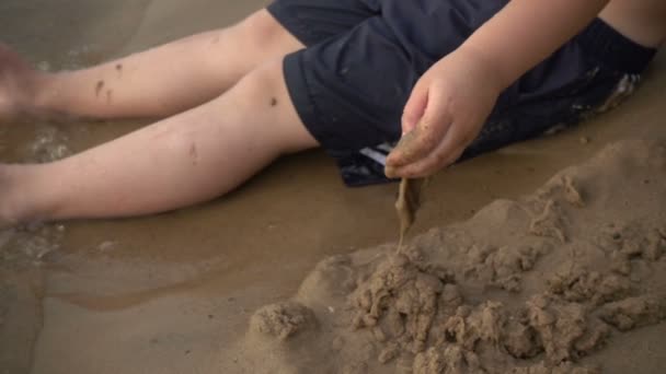 Niño feliz jugando con arena en la orilla — Vídeo de stock