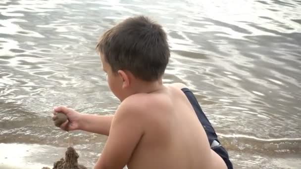 Щасливий хлопчик грає з піском на березі — стокове відео