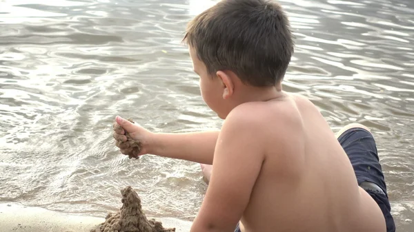 Menino feliz brincando com areia na costa — Fotografia de Stock