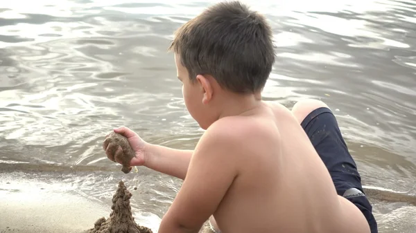 Szczęśliwy chłopiec bawi się piasek na brzegu — Zdjęcie stockowe