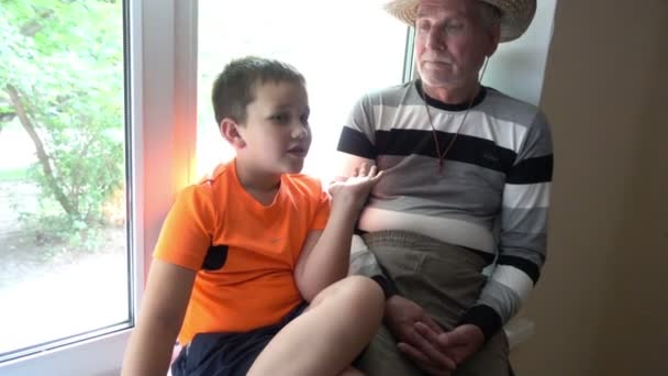 Opa en kleinzoon praten, lachen en kijken naar de camera - de oude man en het kind — Stockvideo