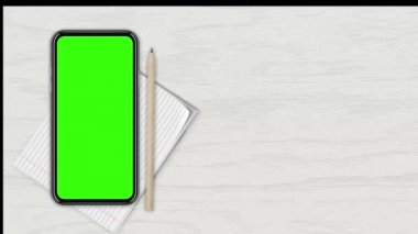 Beyaz ahşap bir tezgaha karşı üst manzaralı boş yeşil ekranlı akıllı telefon. 4K animasyon, tasarım ekranındaki sunum için hareketleri izler. 3 Boyutlu Hazırlama