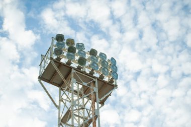 Sahanın üzerinde projektörler ve arka planda bulutlar.