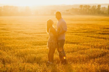 Romantik ilişki kavramı. Mutlu bir çift silueti batan güneşin altında bir tarlada sarılıyor.. 