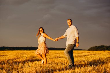 Romantik ilişki kavramı. Gün batımında bir tarlada yürüyen aşıklar gün batımında el ele tutuşuyorlar. Sonbahar mevsimi. 