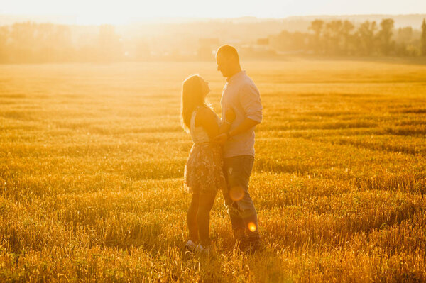 Концепция романтических отношений. Счастливая пара силуэт в поле в лучах заходящего солнца обнимает. 