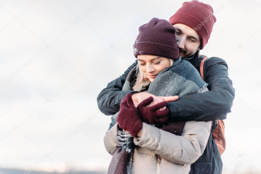 Happy loving couple walking in snowy winter, spending Christmas vacation together. Young hipster couple hugging each other in winter park. Winter love story, a beautiful stylish young couple.