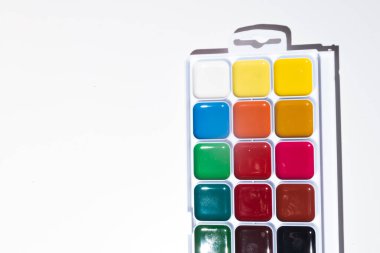 Bir kutunun içindeki suluboya resimlerinin üst görüntüsü, beyaza izole edilmiş. Okul konseptine geri dönelim. Resim okulu ya da sanat mağazası kavramı. Çocuklar ve yetişkinler için hobi kavramı. Minimalizm, üst görünüm, kopyalama alanı.