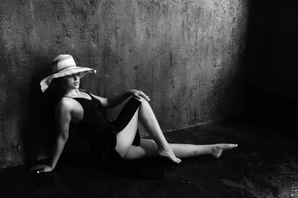 サイドモノクロポートレートの女性で白い帽子で暗い部屋に座って — ストック写真