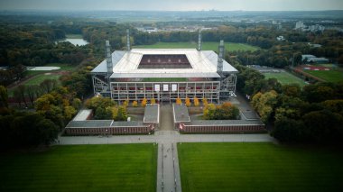 Cologne, Germany - 12 October, 2025: aerial view of a modern Muengersdorf football stadium aligned with a central walkway and lawns, set within a forested urban park. No people. Symmetry