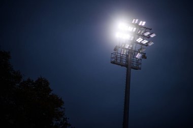 Karanlık akşam gökyüzüne karşı parlak stadyum projektör kulesi. Gece sporları etkinlikleri için güçlü aydınlatma, minimal kompozisyon.