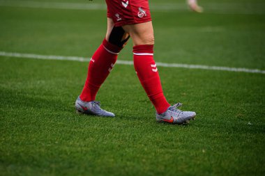 COLOGNE, ALMANY - 16 EKİM, 2025: Oyuncular yeşil alanda yürüyen kırmızı takımlı alt gövde, gri kramponlar görünür. Temiz futbol detayı, kenar çizgisi perspektifi.