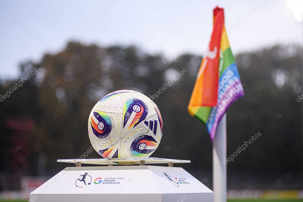 COLOGNE, GERMANY - 16 OCTOBER, 2025: Frauen-Bundesliga match ball on branded stand with rainbow corner flag in rain. Inclusive stadium scene before kickoff.